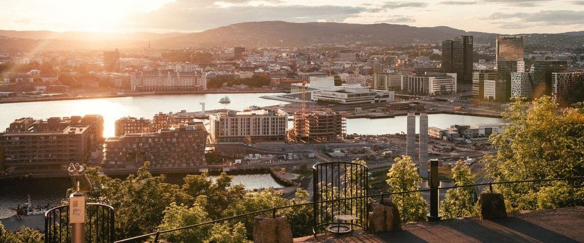 City view in southern Norway at sunset, with waterfront, buildings and surrounding hills.
